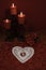 Heart shaped dollie and gemstone, three red candles in metal holders and bouquet of red roses on wooden table.