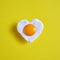 Heart shaped fried egg on yellow background, for the world egg day.