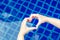 heart shaped hands on background of pool. Female hands folded in shape of heart in front of water