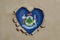 Heart shaped hole torn through paper, showing Maine flag