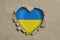 Heart shaped hole torn through paper, showing Ukrainian flag