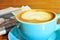 Heart-shaped pattern in a cup of cappuccino with newspaper and wooden table in background