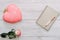 Heart shaped pink mousse cake on table with rose and notepad.