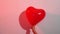 A heart shaped red balloon in hand against a white wall in colored light