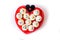 Heart shaped red dish full of frosted white cupcakes and black c