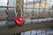 Heart-shaped red love padlock chained to bridge
