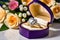 A heart-shaped ring with a large diamond in a gift box on the background of a bouquet of flowers. Jewelry is a