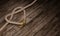 Heart shaped rope knot and golden ring on wooden surface and plank.