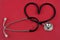 Heart-shaped stethoscope close up on red background