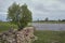 A heart-shaped tree among the remains of a stone structure in the front and the lake in the background. Rural fields, overcast sky