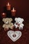 Heart shapped dollie and gemstone, three red candles in metal holoders and red rose, two teddy bears on wooden table