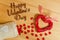 Heart sign Happy Valentine`s Day on a wooden texture, and spilling out of the bag with small glass hearts