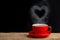 Heart of steam hovering over a red coffee cup of coffee on wooden table with black background