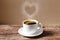 Heart of steam hovering over a red coffee cup of coffee on wooden table with cream wall background
