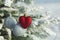 Heart toy with silver balls on a pine branch in the snowy forest.