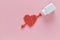A heart was embroidery by arrow shape of medicine pills pouring out of white bottle on pink background. Concept of Valentine`s Day