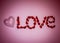 Heart and word love laid out from artificial flowers on a pink background