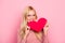 She is a heartbreaker! Close up portrait of jealous young attractive woman with long blonde hair. She is holding a heart and