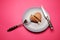 Heartbreaker concept image: heart shaped cookie on plate with fork and knife over pink background