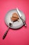 Heartbreaker concept image: heart-shaped cookie on plate with fork and knife over pink background