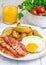 Hearty breakfast with bacon, fried egg, potato and orange juice