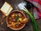 Hearty homemade soup with potatoes, carrots, sausages and olives in a clay bowl on a wooden background.