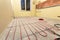 Heating red electrical cable wire installation on cement floor in small new unfinished room with plastered walls. Renovation and