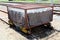 Heavily used rusted metal railway cart closed with strong wire cage on unused part of railway tracks