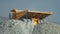 Heavy dump truck finishes to unload the ore and leaves the quarry. View from back.