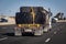 Heavy equipment tires being hauled on a flatbed trailer with straps and a a wide load sign