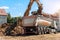 Heavy excavatore machine uploading waste and debris rubble into dump truck at construction site. Building dismantling