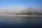 Heavy fog-covered rolling hills wit a reflection on a calm reflective lake water