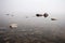 Heavy fog over a lake with clear water and stones.