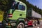Heavy green car carrier truck transports on highway road on summer day against forest and blue sky, logistics business in Europe