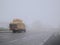 Heavy lorry with tall stack of bale of hay on asphalt road in town in a fog. Bad traffic condition. Agriculture and transportation