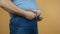 Heavy man trying to fasten jeans pants under a fat stomach, the problem of overeating, obesity