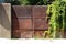 Heavy massive old completely rusted metal closed front yard double doors mounted on concrete fence walls covered with crawler