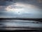 Heavy rain falling on a dark beach at low tide with dramatic storm clouds reflected on the wet sand with a line of footprints