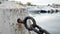 Heavy, rusted, metal chain is secured to a white concrete bollard