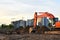 Heavy tracked excavator at a construction site on a background of a residential building and construction cranes on a sunny day