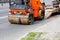 Heavy vibrating road roller is unloaded from a low platform trailer and drives onto the carriageway