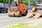 Heavy vibrating road roller is unloaded from a low platform trailer and stands on the roadway