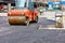 A heavy vibratory roller compacts hot asphalt on the roadway on a clear sunny day