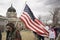 Helena, Montana - April 19, 2020: A woman at a protest holding an American flag walking with a large group of people protesting