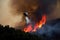 helicopter flying over wildfire, dropping water to extinguish flames