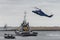 Helicopter hovering over a tug boat in the middle of an expansive body of water.