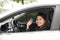 Hello! Beautiful young cheerful woman looking at camera with smile and waving while sitting in her car