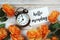 Hello Monday card and alarm clock with orange flower decoration on wooden background