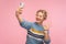 Hello! Portrait of positive pretty woman with curly hair in warm sweater waving hand to smartphone and taking selfie