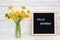 Hello Saturday words on black letter board and bouquet of yellow dandelions flowers on table against white brick wall. Concept